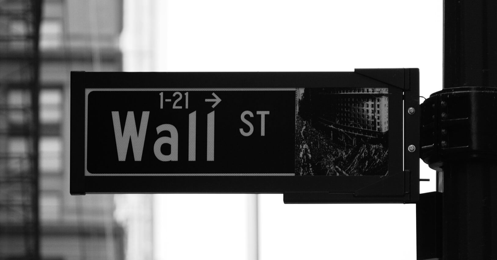 Czarno-białe zdjęcie tablicy ulicznej z napisem Wall St w Nowym Jorku, reprezentującej światowe centrum finansowe i giełdowe.